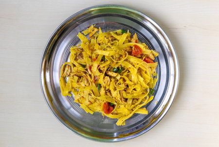 Homemade delicious chicken flat noodles served on a steel plate with a light wooden backdrop. Top...