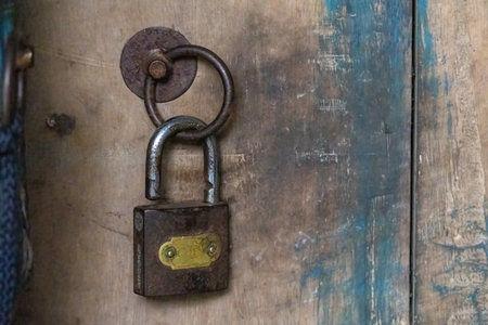 A close-up shot of an old, rusty door lock, hanging unlocked on a weathered wooden door.の写真素材