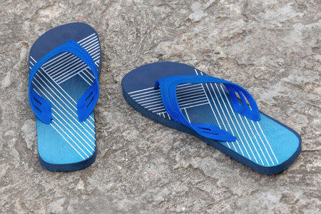A pair of stylish navy blue flip-flops on a concrete floor. These light, sandal-like shoes are...