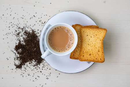 Hot milk tea with bubbles in a teacup and crispy rusk biscuits. Fresh and dried tea leaves on a...