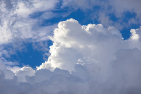 Gorgeous fluffy white and soft gray clouds dominate a clear, bright blue sky. An expansive,...