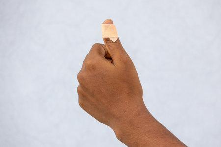 Injured female thumb finger close-up, cut by a knife, with an adhesive bandage being applied. Focus on the sticking plaster on the wounded hand, showing first aid and recovery.の写真素材