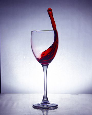 splash of the drink in the glass on the high leg on colored backgroundの写真素材