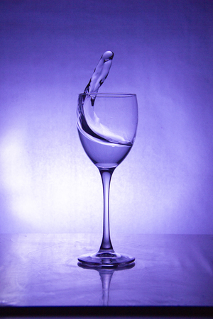 splash of the drink in the glass on the high leg on colored backgroundの写真素材