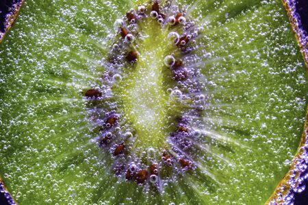 a slice of fresh juicy tasty kiwi under water is covered with small air bubbles macro shotの写真素材