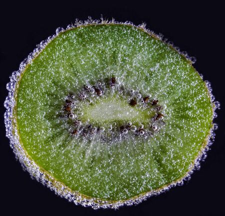 a slice of fresh juicy tasty kiwi under water is covered with small air bubbles macro shotの写真素材