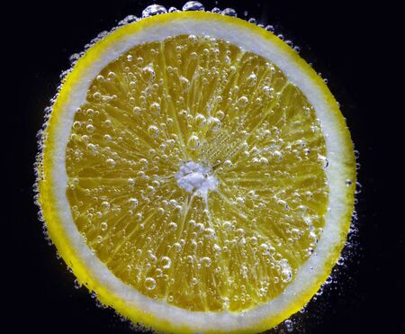 a slice of fresh juicy orange under water is covered with small air bubblesの写真素材