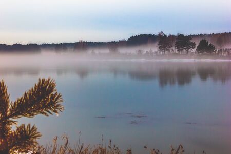 the river with snow-covered banks at sunset is covered with thick fogの写真素材
