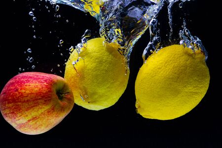 ripe yellow lemons and red Apple fall into the water and create beautiful water swirls and bubbles on a black backgroundの写真素材
