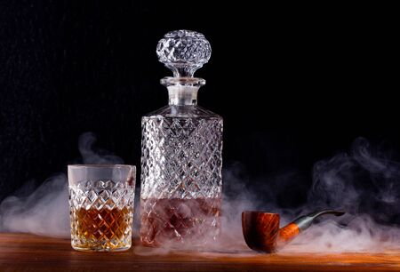 a fluted glass and decanter of whisky and a Smoking pipe on the tableの写真素材