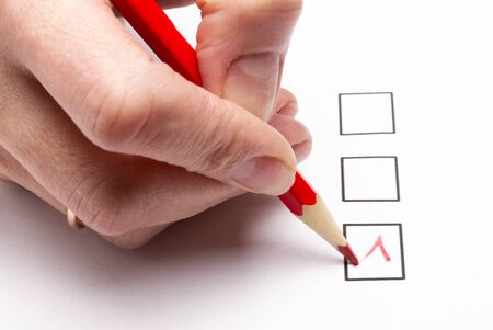 hand holding a red pencil makes a choice in the voting questionnaire