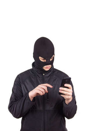 a man in a black mask with a cell phone and a laptop is engaged in Internet fraudの写真素材
