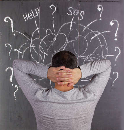 a man thinks and behind him on the wall are painted with chalk questions and thoughts