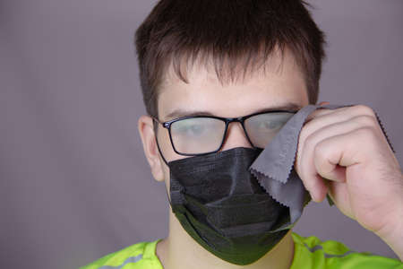 a masked person wipes their fogged glasses with a rag
