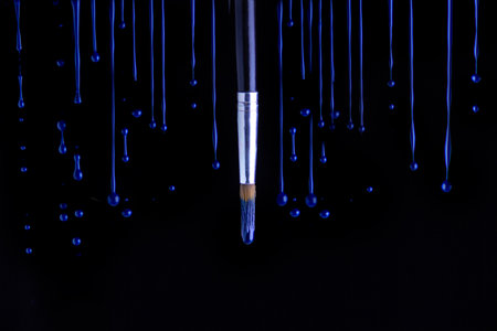 blue paint drips around the brush on a black backgroundの写真素材