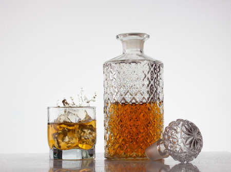 a crystal decanter of whiskey next to a glass of whiskey with scattered splashesの写真素材