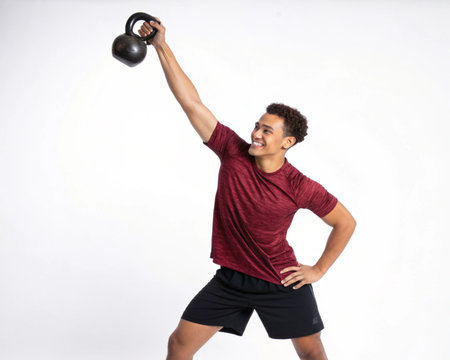 A fit man in athletic wear smiles while performing a kettlebell overhead press, showcasing strength and determination.の素材