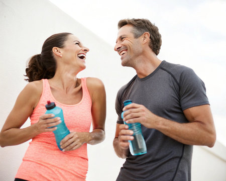 A happy, active middle-aged couple shares a laugh while holding water bottles, radiating health and vitality.の素材