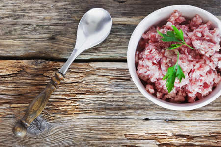 fresh minced meat in a white bowl on the old wooden background. semifinished meat