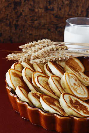 freshly baked fritters on a plate, wheat stalks and glass of milk on the table. traditional european...