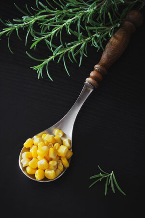 spoon full of pickled corn and rosemary on a black wooden background. home preservation.health and diet foodの写真素材