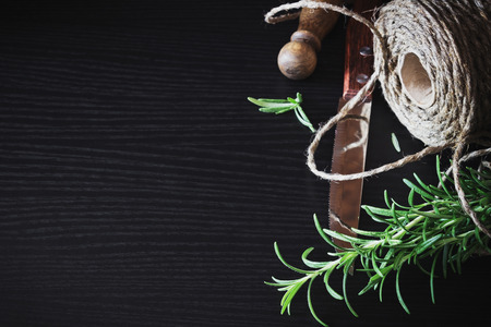 twig of fresh rosemary, a kitchen knife and a skein of of flax rope on black wooden table.  copy space background. healthy food from gardenの写真素材