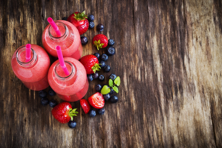 strawberry smoothie in a bottle and ripe garden and forest berries on the wooden background. health and diet concept. selective focus. copy space backgroundの写真素材