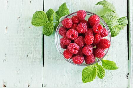 ripe juicy raspberries in a glass bowl on a colored wooden background. from his garden berries. top view. health and diet foodの写真素材