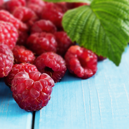 Ripe tasty raspberries on a blue wooden background. Square image. Healthy and diet food. Selective...