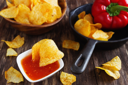 Potato chips and chili sauce on an old wooden table. Unhealthy food. Selective focusの写真素材