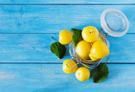 Ripe yellow plums in a glass jar on a blue wooden background. View from above. Bio healthy food background. Organic fruits. Copy space for you textの写真素材