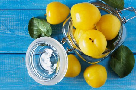 Ripe yellow plums in a glass jar on a blue wooden background. View from above. Bio healthy food background. Organic fruitsの写真素材