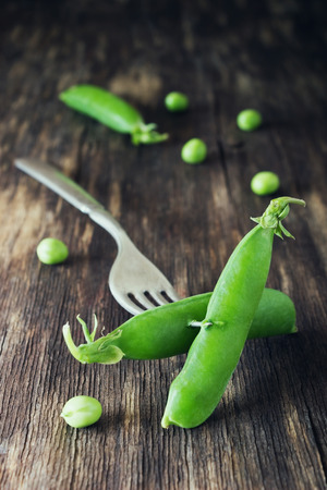Pods ripe green peas skewered on a fork on a vintage wooden background. Toned image. Healthy food concept. Organic vegetables. Selective focusの写真素材