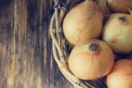 Ripe onion in a vintage basket on a wooden table. Close-up. Copy space. Selective focus. Toned image. View from aboveの写真素材
