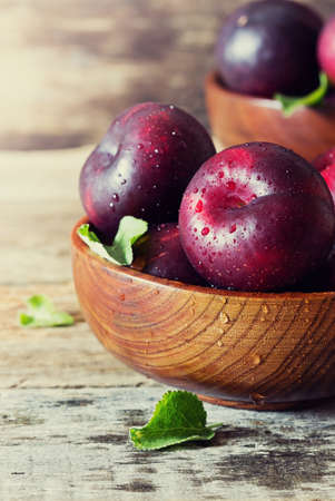 Ripe organic plums in a wooden bowl. Health and diet food. Selective focus. Toned imageの写真素材