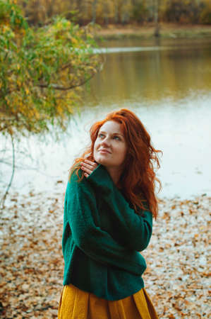 Portrait of a beautiful red-haired girl with freckles and blue eyes which in autumn parkの写真素材