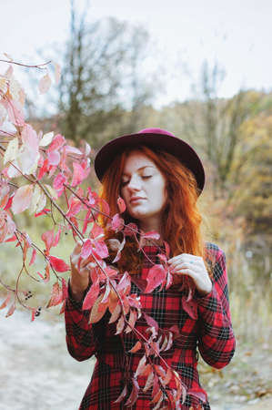 Redhead girl in red dress and hat walking in autumn forest