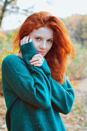 Portrait of a beautiful red-haired girl with freckles and blue eyes which in autumn parkの写真素材