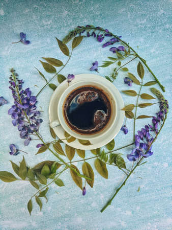 Cup of morning hot coffee on a blue background with beautiful white flowers as a daily ritual