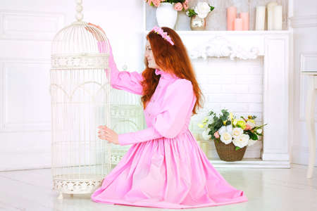 Redhead pretty woman in a pink dress sitting in sunny spring day at studio and dreaming about Woman day.の写真素材