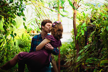Romantic picture of lovely couple on a date in casual clothes, in beautiful glass greenhouse. Happy man and woman hugging and holding hands, spending time together. Valentine's Day.の写真素材