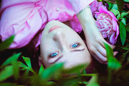 Portrait of young attractive woman in spring garden with blooming pink peonies. Spring background. Woman's Day. Greeting card.の写真素材