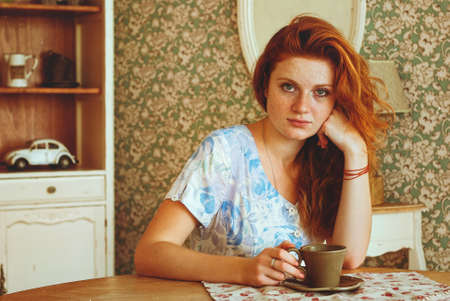 Portrait of young redhead woman with freckles drinking coffee in sunny morning at home. Natural beauty. Woman's Day. Still life.の写真素材
