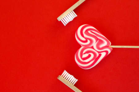 Festive red background. Sweet heart shaped candy. And two toothbrushes like a symbol of love. Valentine's Day. 14 of February. Ideas of gifts. Flat lay, top view.の写真素材