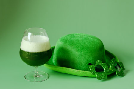 Happy St Patrick's Day concept. Glass of green beer and party glasses in green background. Greeting...