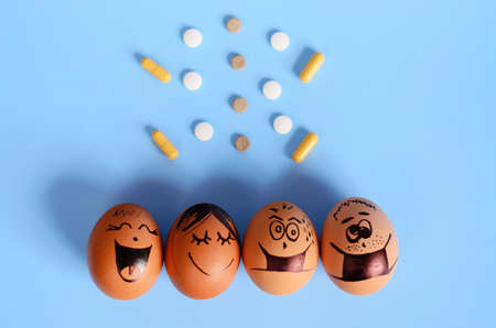 Creative Easter chicken eggs with doodle faces wearing medical masks with pills on blue background. Flat lay, top view, mockup, copy space.の写真素材
