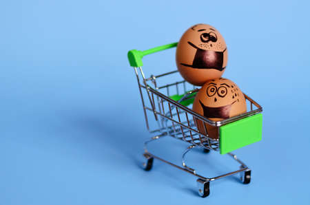 Creative Easter chicken eggs on mini shopping cart with doodle faces wearing medical masks on blue...