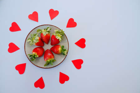 Festive blue background. Red paper hearts and fresh strawberries on a plate. Love. Valentine's Day. Food backgrounds. Creative greeting card. Flat lay, top view.の写真素材