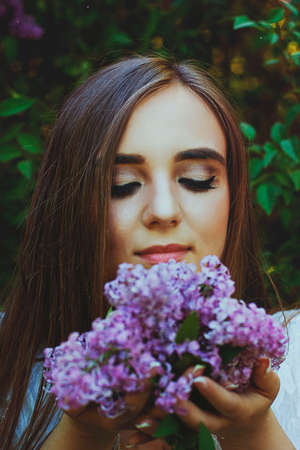 young attractive woman in long dress in spring garden with bouquet of purple lilacs. Sunset light. Spring background. International Woman's Day. Natural beauty.の写真素材