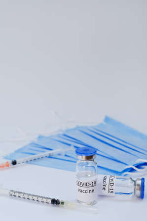 Creative ideas of vaccination concept. Top view of syringe with medical masks and vaccine vial glass bottles for vaccination against COVID-19. Coronavirus pandemic. Copy space.の写真素材